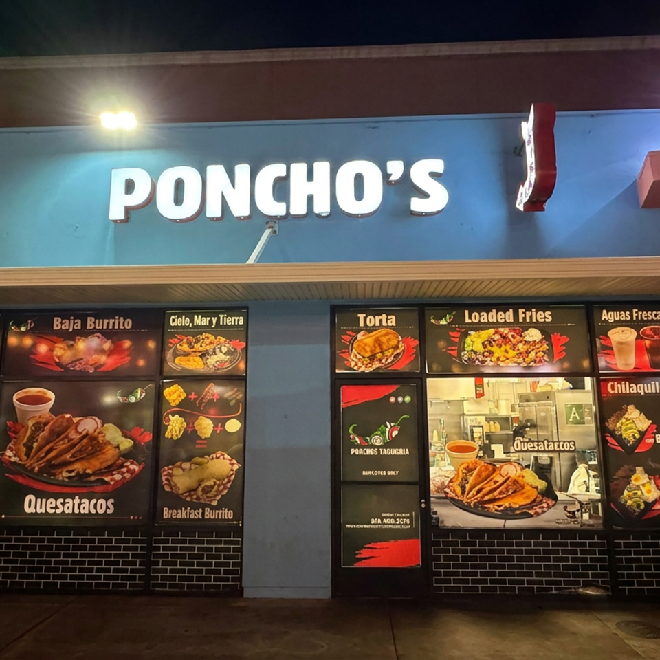 Nighttime exterior of Poncho’s Mexican restaurant, featuring illuminated signage and colorful menu panels displaying tacos, burritos, quesatacos, fries, and aguas frescas.
